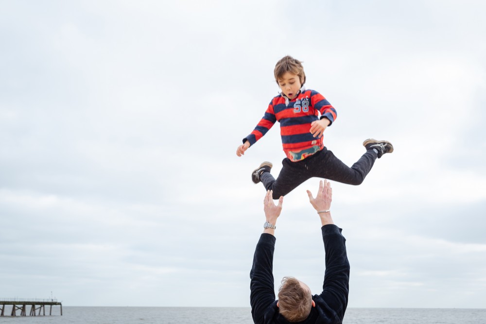 A boy being thrown into the air by his uncle on a family photoshoot at Lowestoft Beach