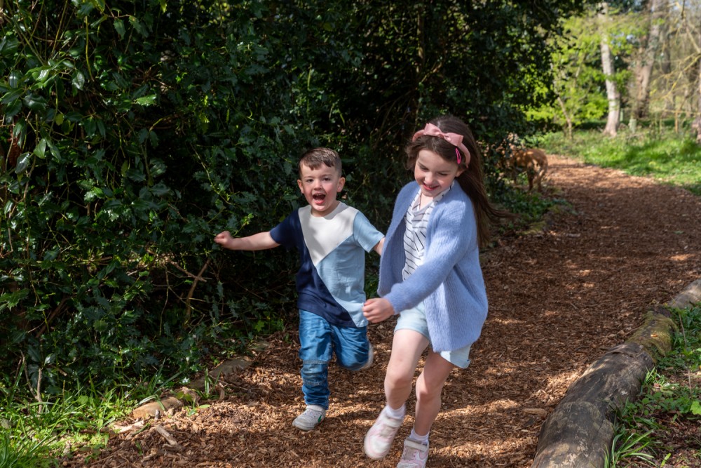 two children running through the woods holding hands and laughing